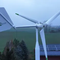 Biała turbina wiatrowa Falcon z zielonymi akcentami na tle pól i dachu z panelami słonecznymi.