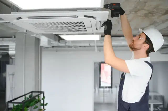 Instalator klimatyzacji montuje jednostkę sufitową w biurze.